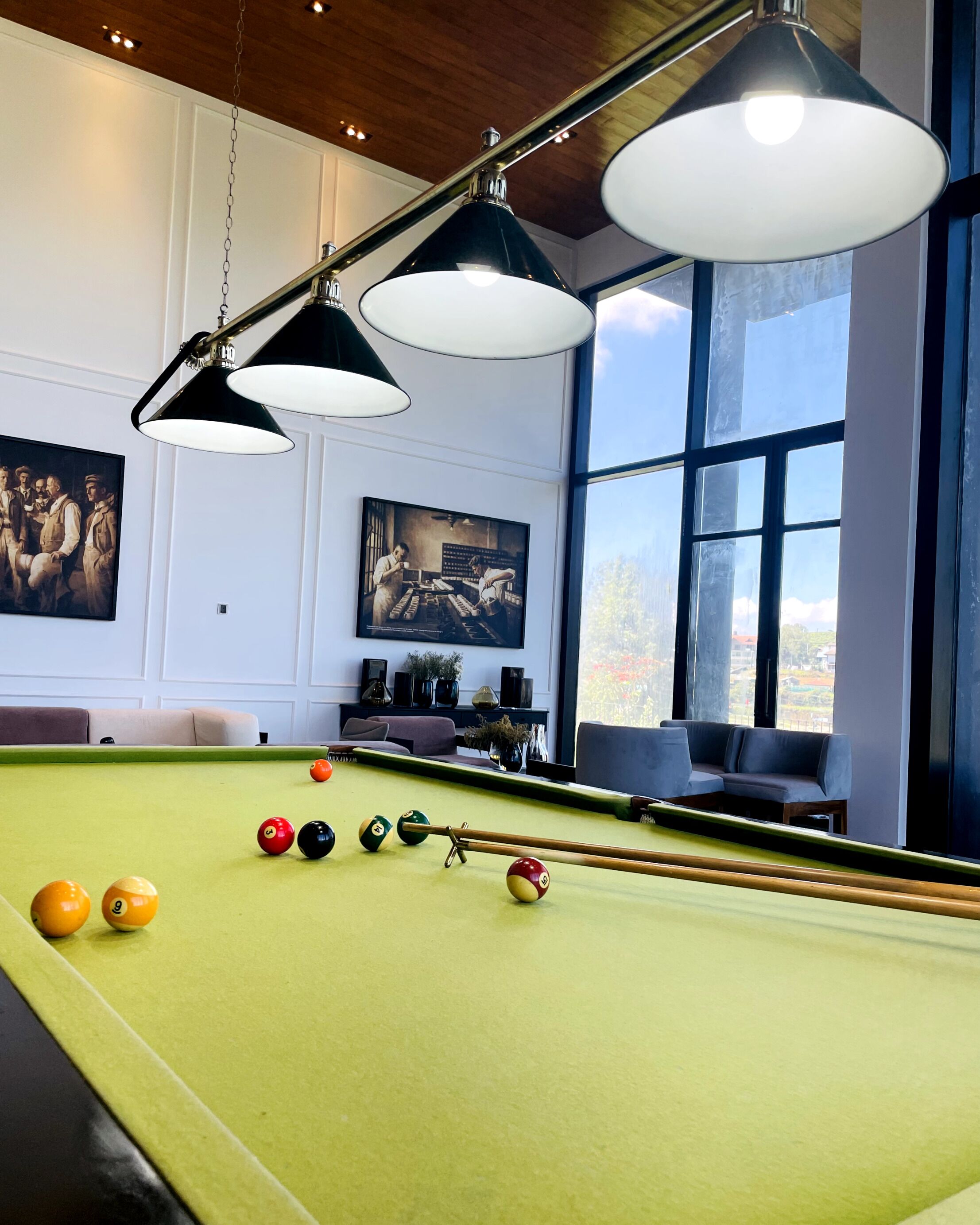 A pool table with balls, a sofa, and two paintings on the wall.