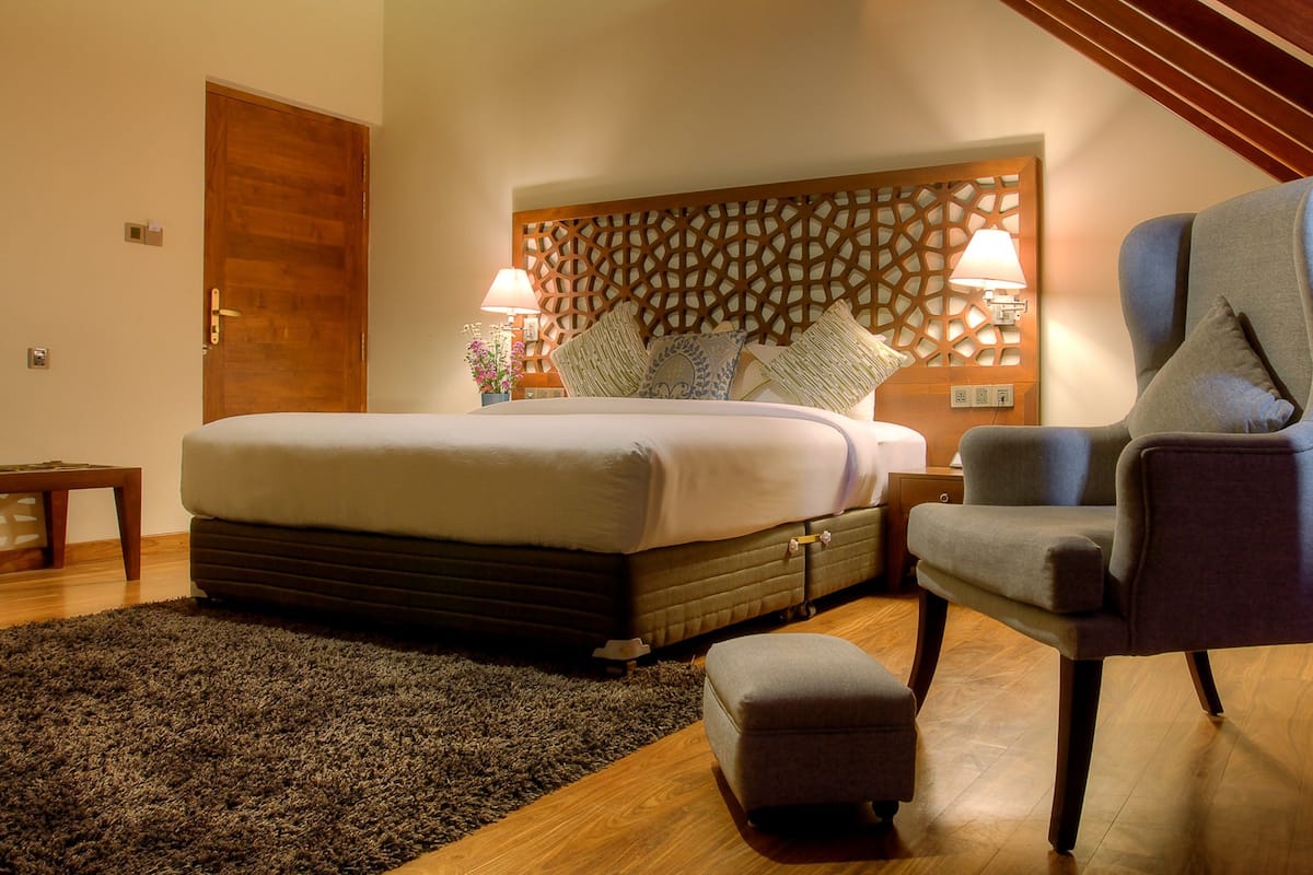 A bedroom with a large bed, a chair, a small table, and a decorative headboard.