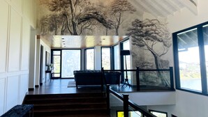 Un interior espacioso con techo alto, ventanas grandes y una escalera que conduce a un nivel superior.