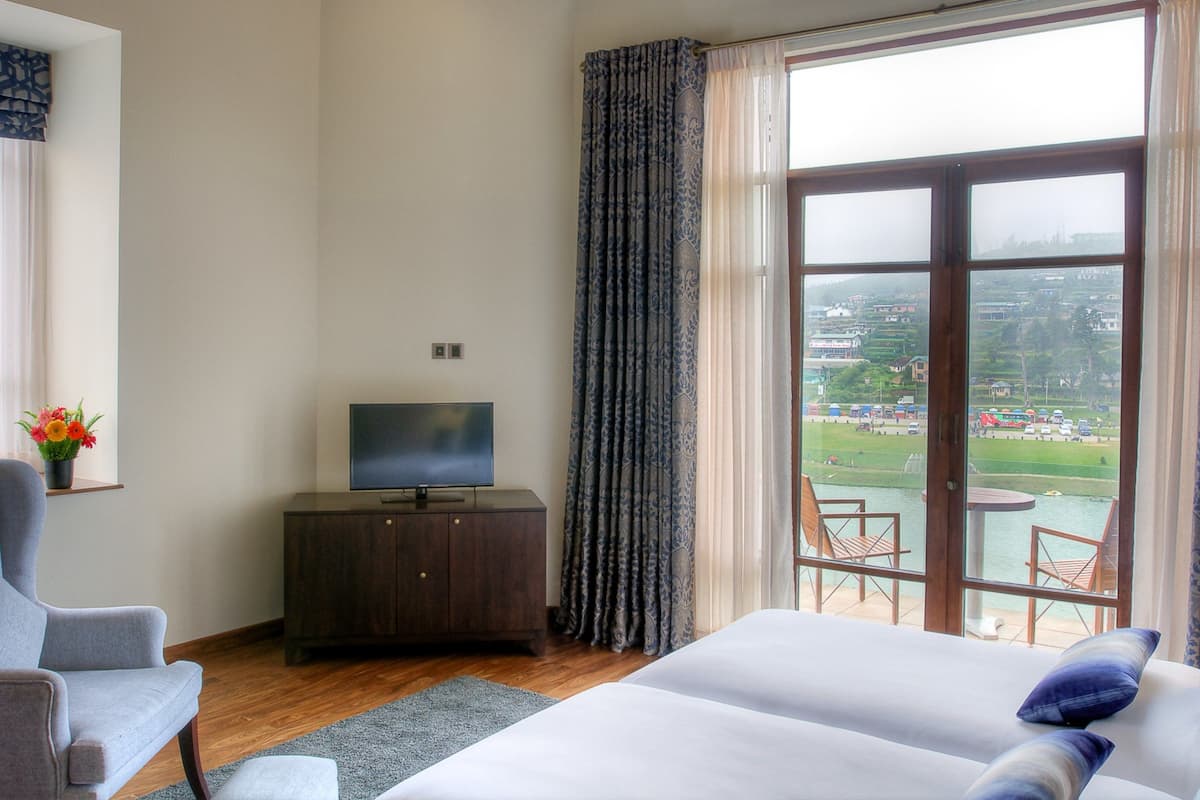 A hotel room with a bed, a TV on a wooden cabinet, a chair, and a view of a body of water and buildings.