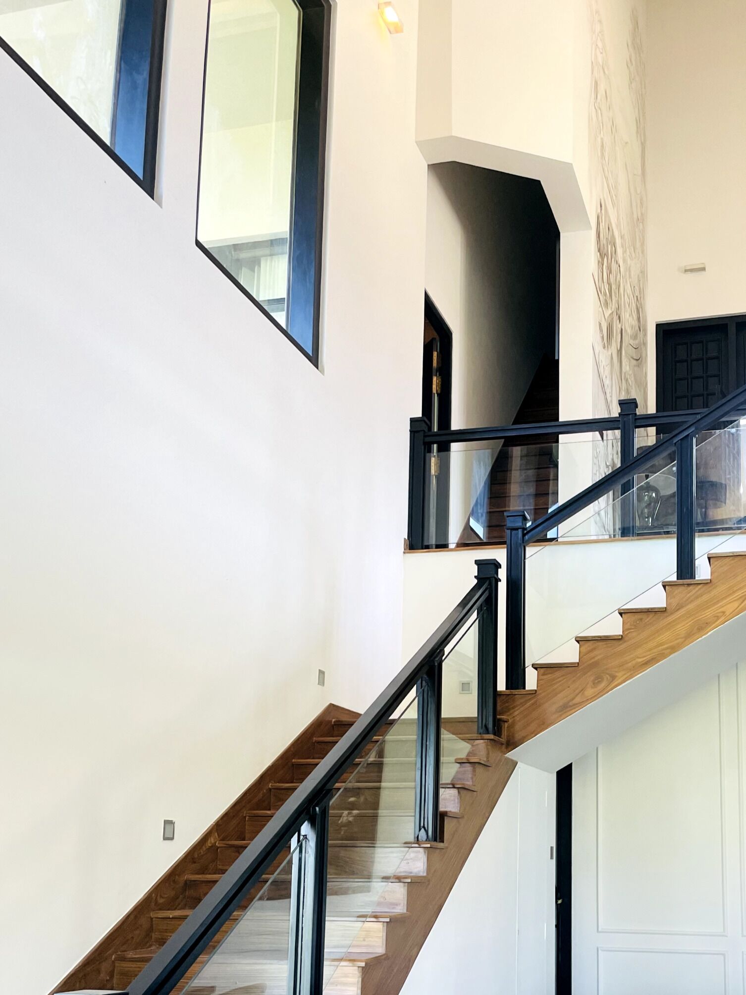 A modern staircase with glass railings and wooden steps, leading to a landing with a door.