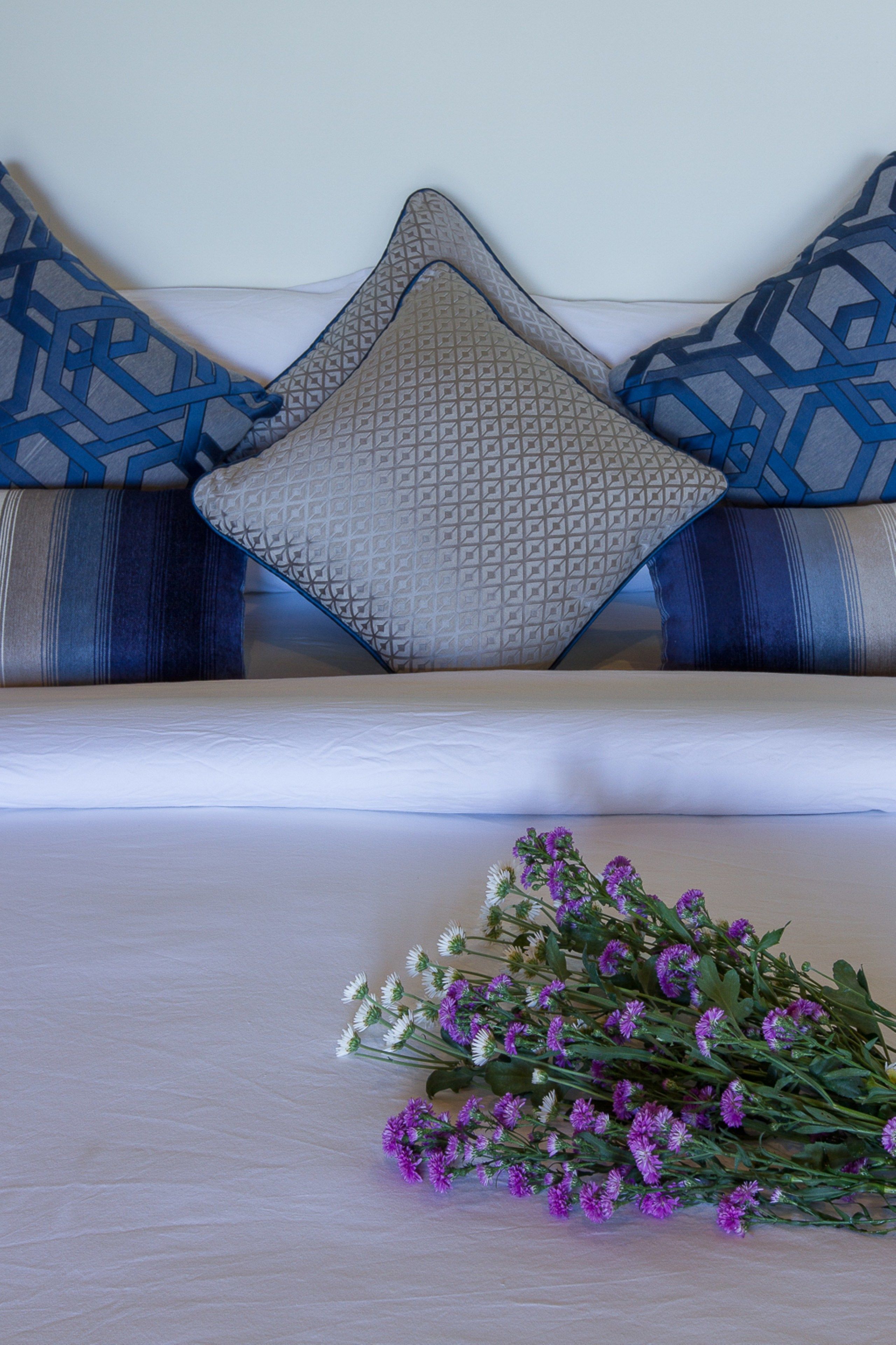 A bed with a white sheet, a grey pillow with a geometric pattern, and a blue pillow with a similar design.