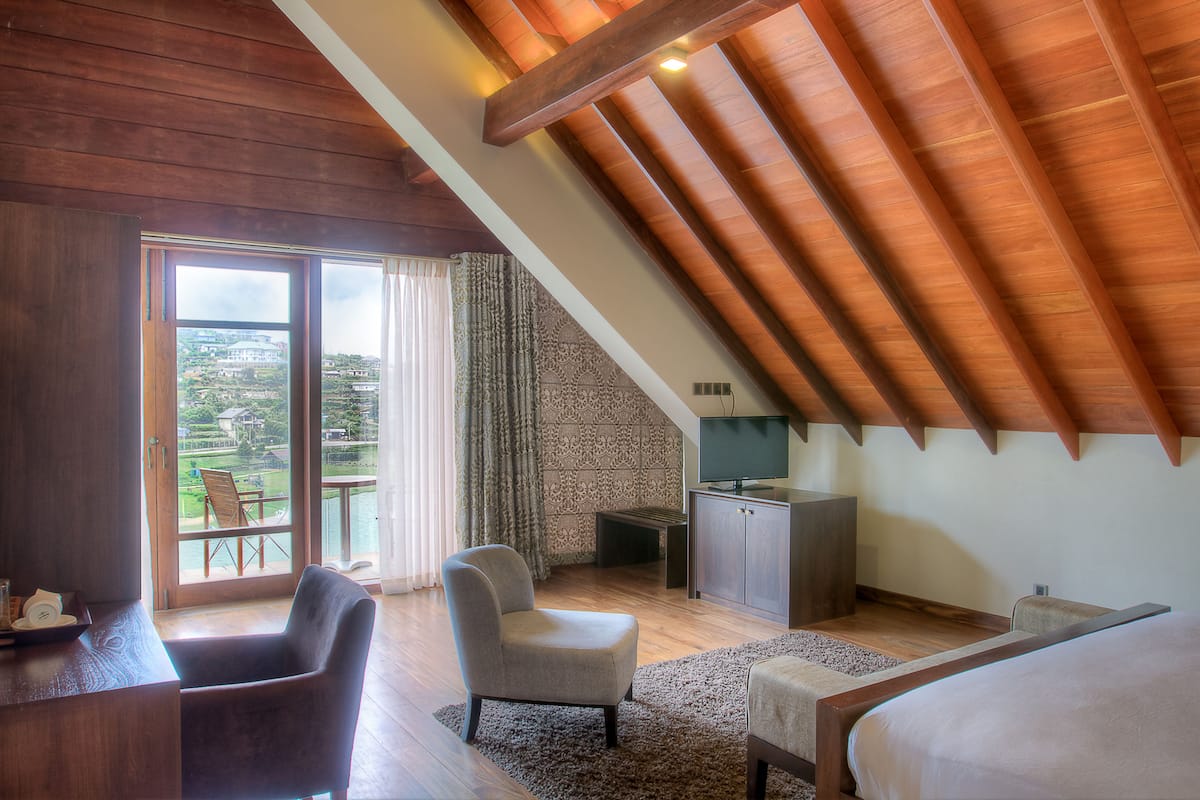 A bedroom with a sloped ceiling, a large window, a bed, a desk, and a chair.