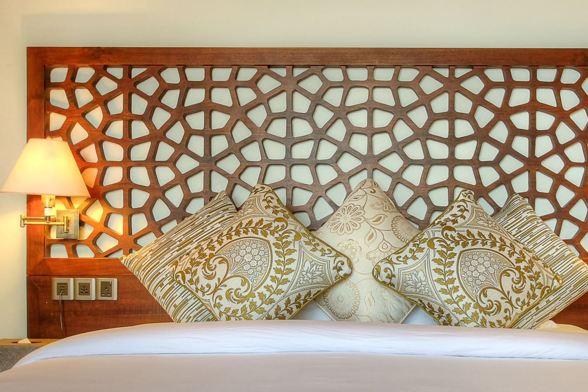 A bed with a wooden headboard featuring a geometric pattern, two bedside lamps, and decorative pillows.