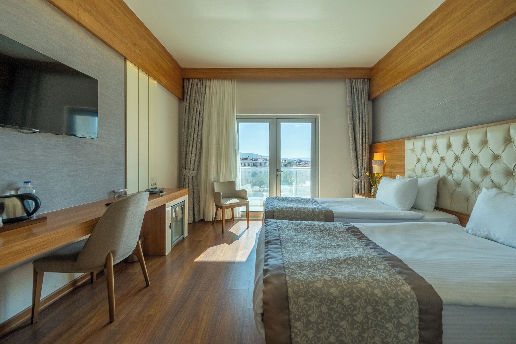 Habitación de hotel con dos camas, un escritorio, una silla, un televisor y vistas a la ciudad.