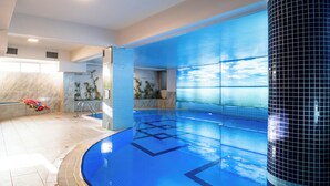An indoor swimming pool with clear blue water, tiled walls, and a large cylindrical column.