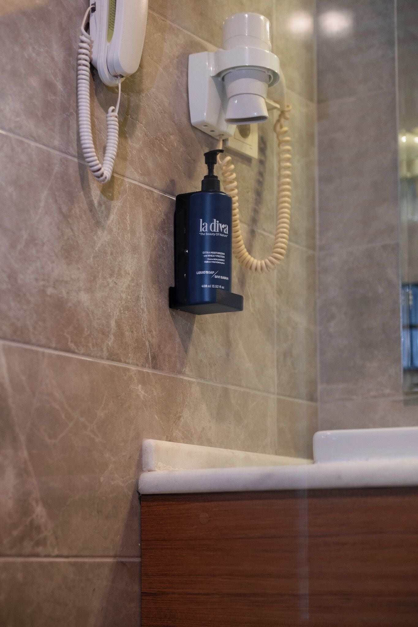 A bathroom with a telephone, a hairdryer, and a bottle of La Divia body wash.