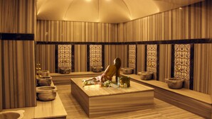 A spa room with a large massage table, multiple stone basins, and a patterned wall design.