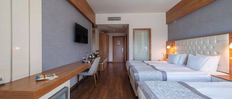 A hotel room with a wooden desk, two beds, a TV, and a minibar.