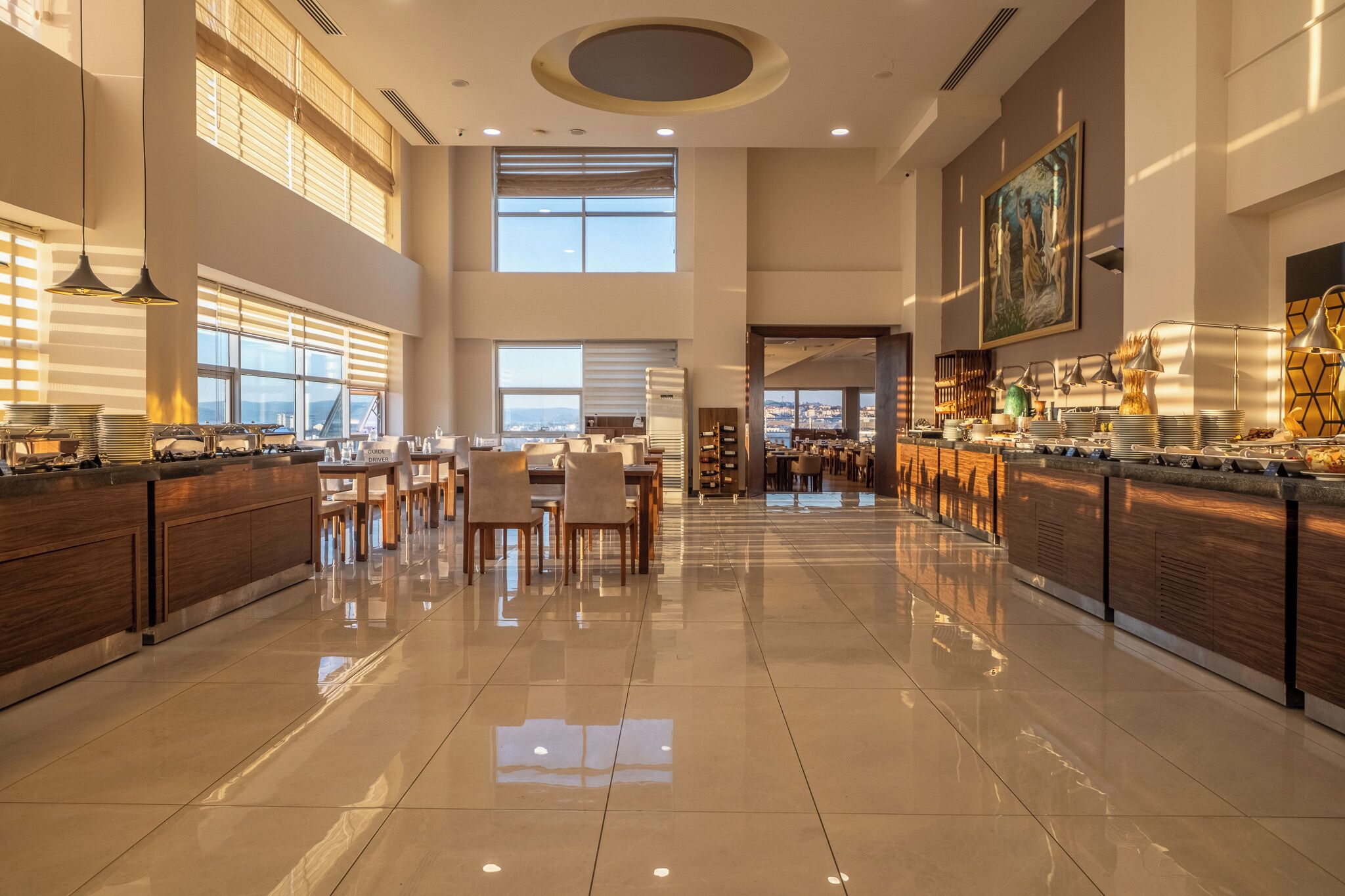 A spacious, well-lit hotel lobby with high ceilings, large windows, and a polished floor.