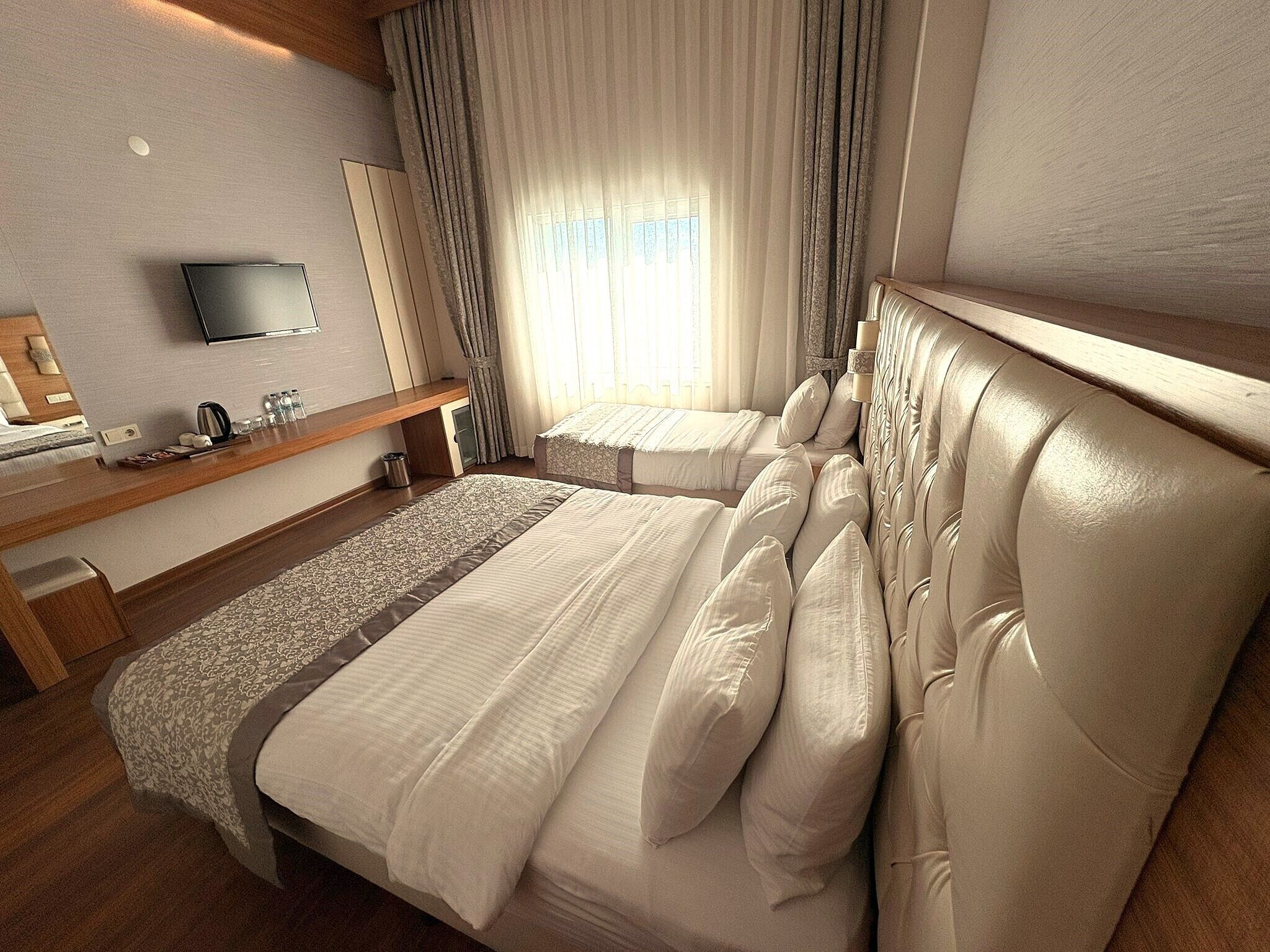 Habitación de hotel con dos camas, televisor, escritorio con artículos de aseo y ventana con cortinas.