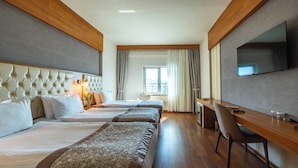 A hotel room with two beds, a desk, a chair, a TV, and a window with curtains.