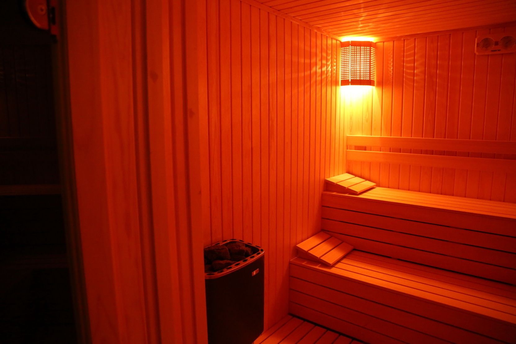 A sauna with wooden walls and benches, a light fixture, and a trash bin.