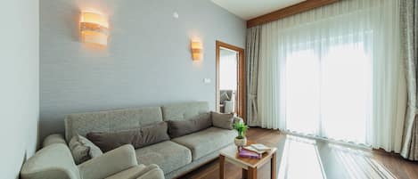 Una sala de estar moderna con un sofá gris, una mesa de centro de madera y un ventanal con cortinas translúcidas.