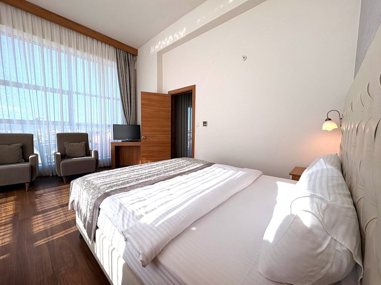 Habitación de hotel con una cama grande, dos sillones, un televisor y una mesita de noche.