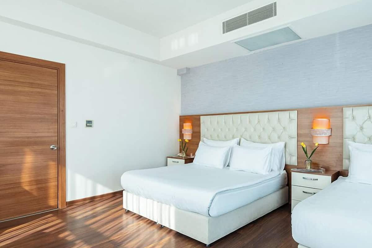 A hotel room with two beds, a wooden floor, a white door, and a light-colored headboard.