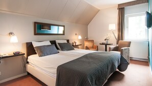 Een hotelkamer met een groot bed, twee nachtkastjes met lampen, een stoel, een klein tafeltje met een plant en een aan de muur bevestigde televisie.