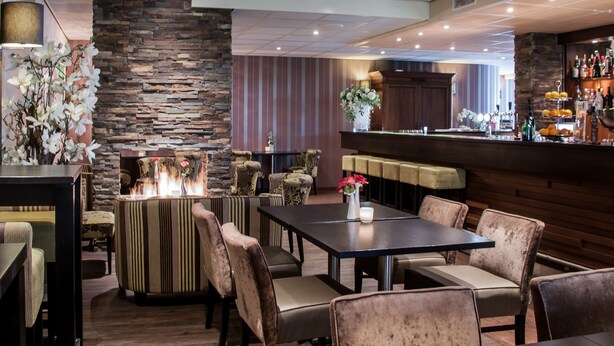 Een restaurant met een stenen muur, comfortabele zitmogelijkheden, een bar en een open haard.