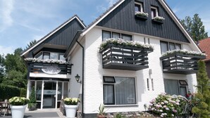 Een gebouw met twee verdiepingen, met een bord voor een restaurant en een hotel. Grote potplanten staan ervoor en er is een fiets geparkeerd.