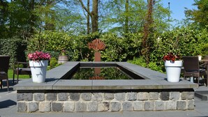 Een stenen fontein met een centrale sculptuur, omgeven door weelderige begroeiing en buitenplaatsen.