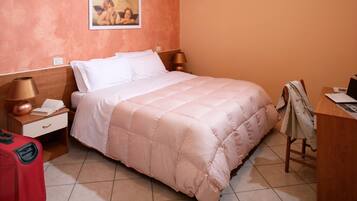 Una camera d'albergo ordinata con un letto, una scrivania, una sedia, una lampada, una valigia e un quadro appeso al muro.