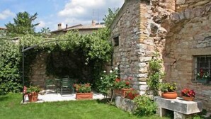 A stone building with a garden area, including a pergola and potted plants. - Il Turrione Appartamenti Vacanze (Assisi)