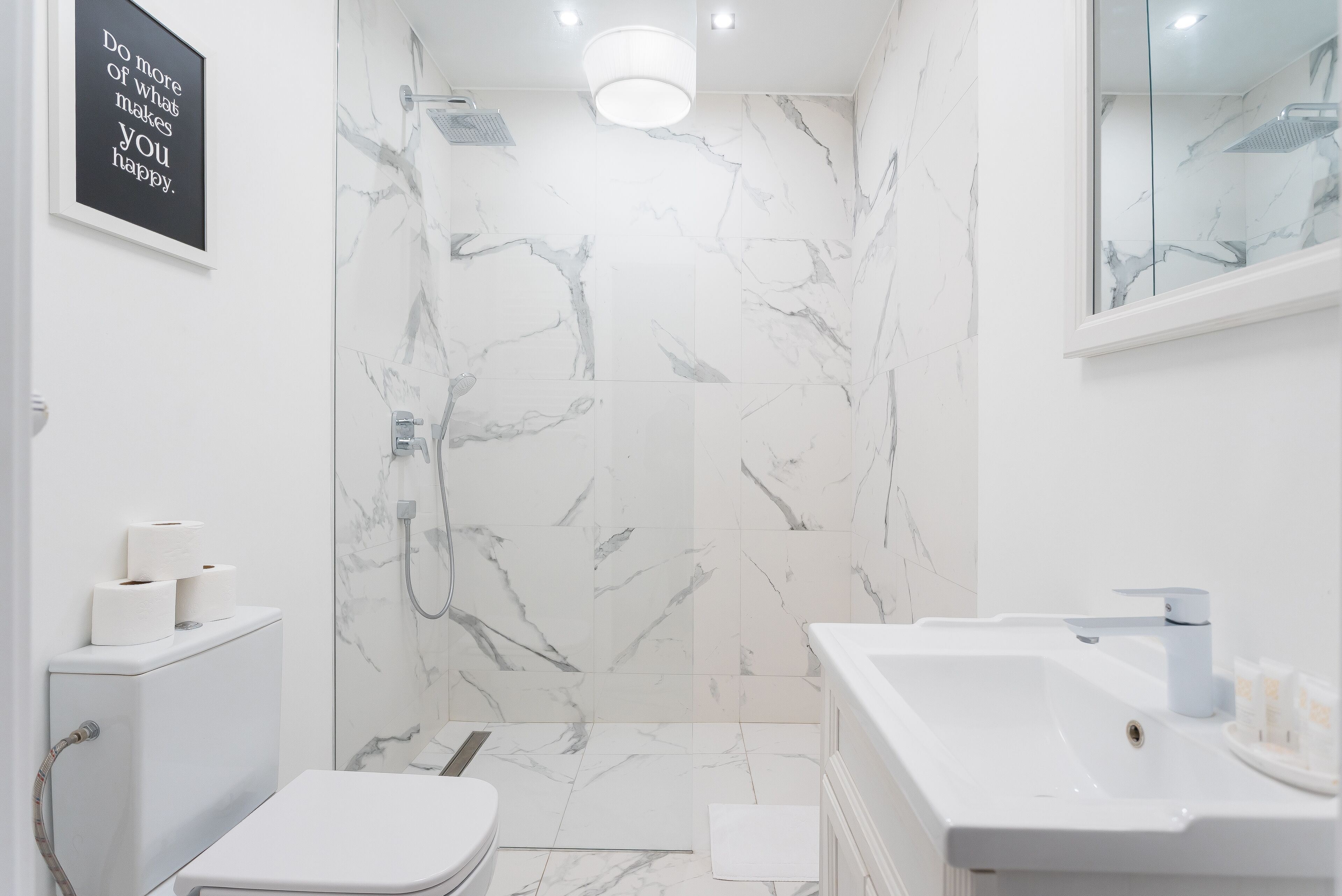 A modern bathroom with a marble shower, a toilet, and a sink.