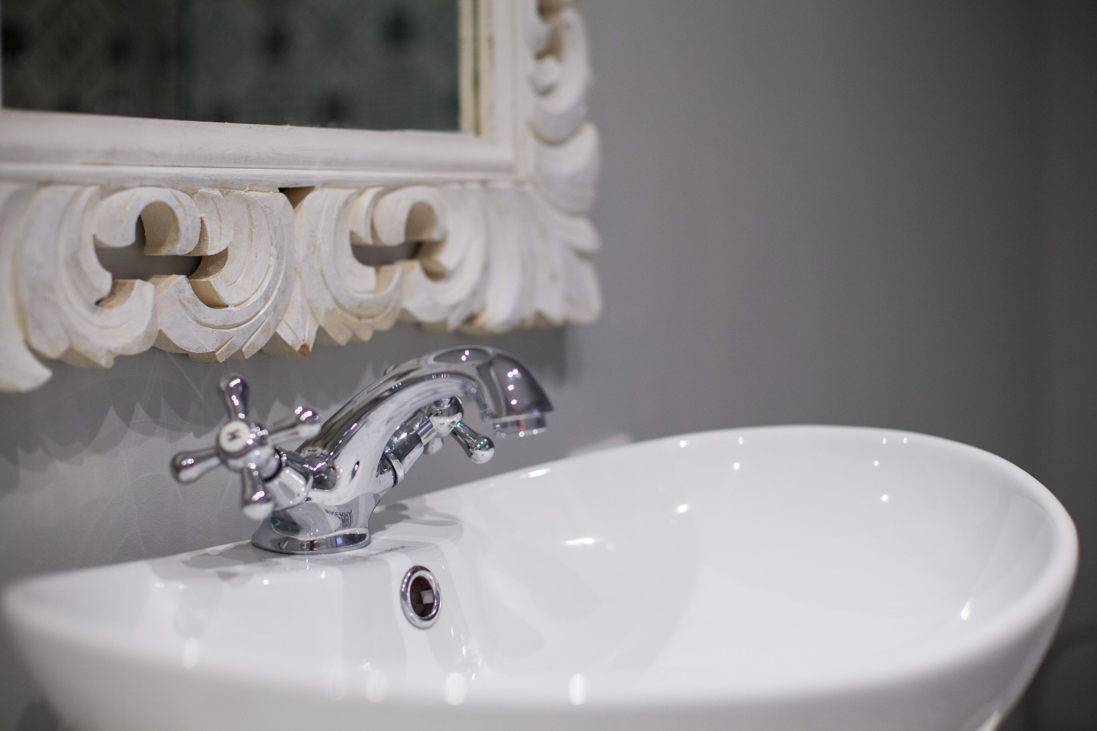 A white bathroom sink with a chrome faucet and a mirror above it.
