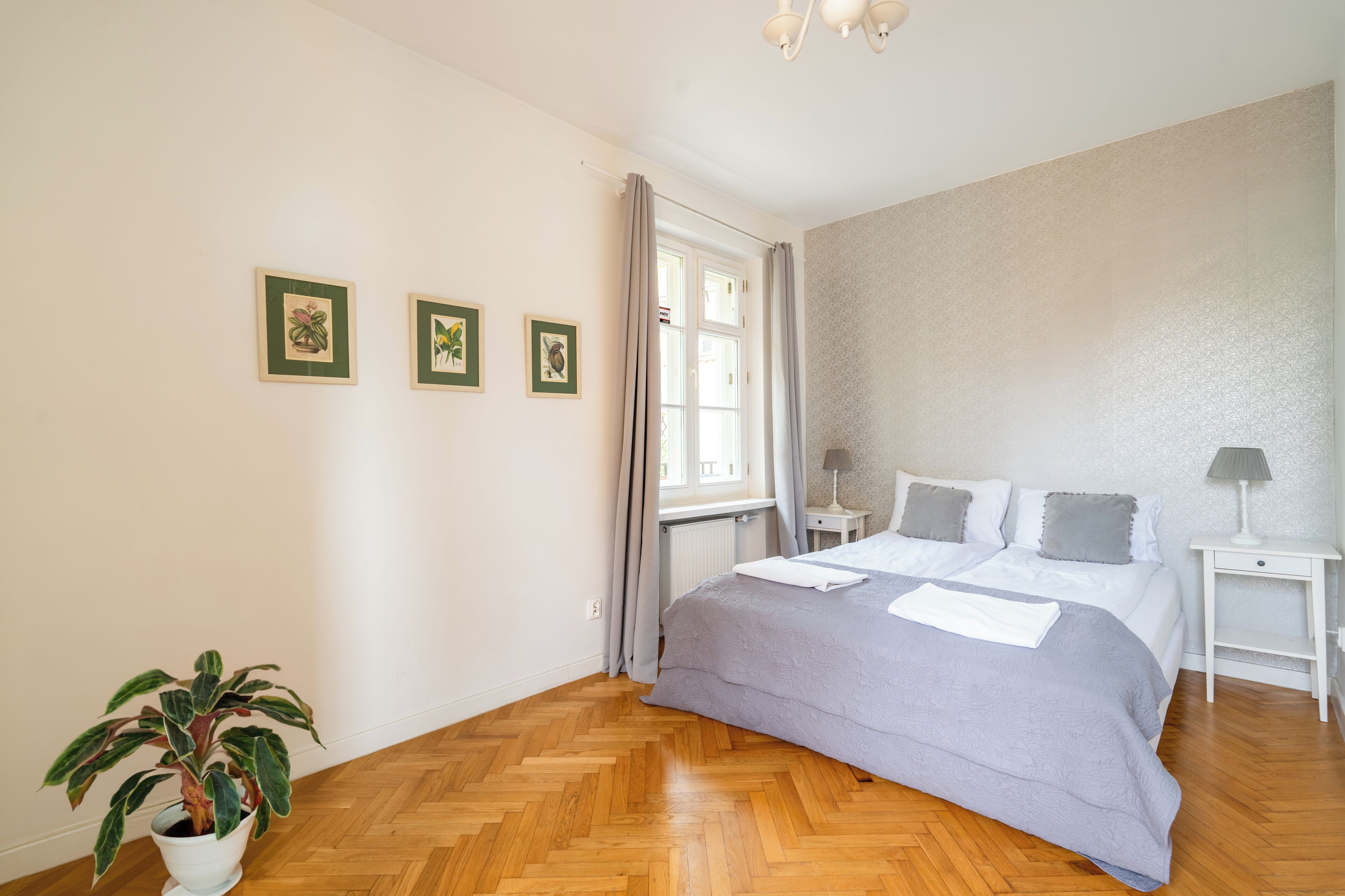 Een slaapkamer met een bed, een potplant en drie ingelijste foto's aan de muur.