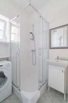 A modern bathroom with a glass-enclosed shower, a white sink, and a built-in washing machine.