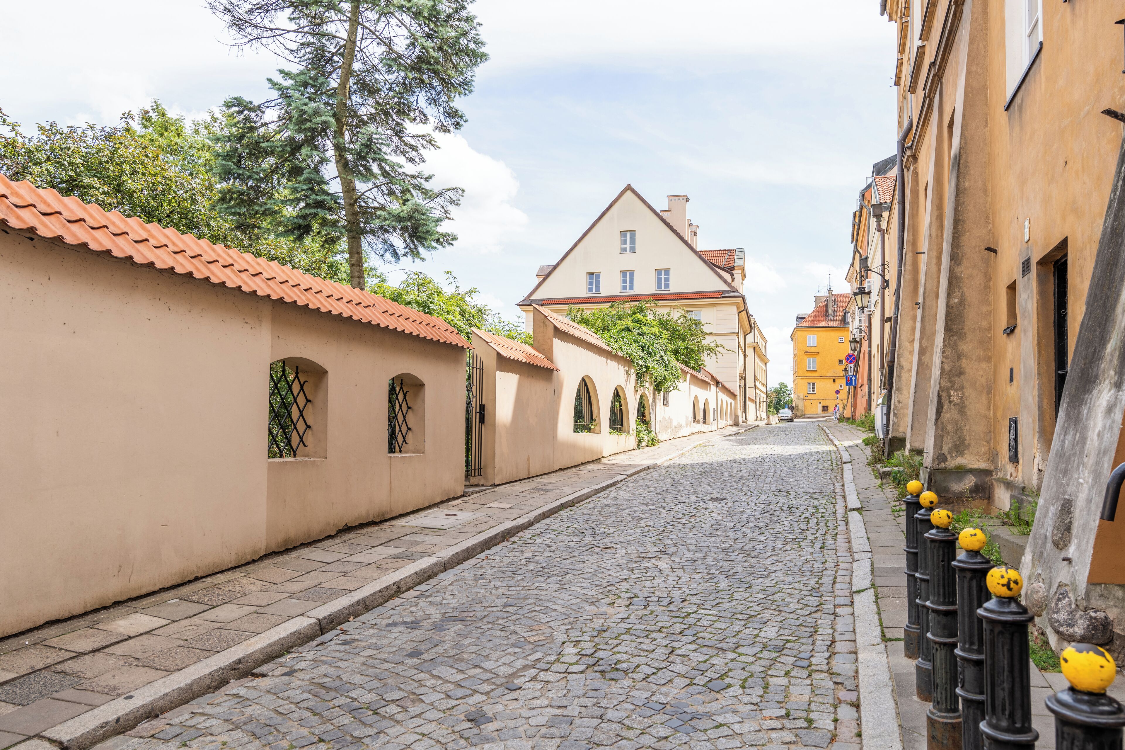 A cobblestone street lined with buildings, some with arched windows and a yellow building in the distance.