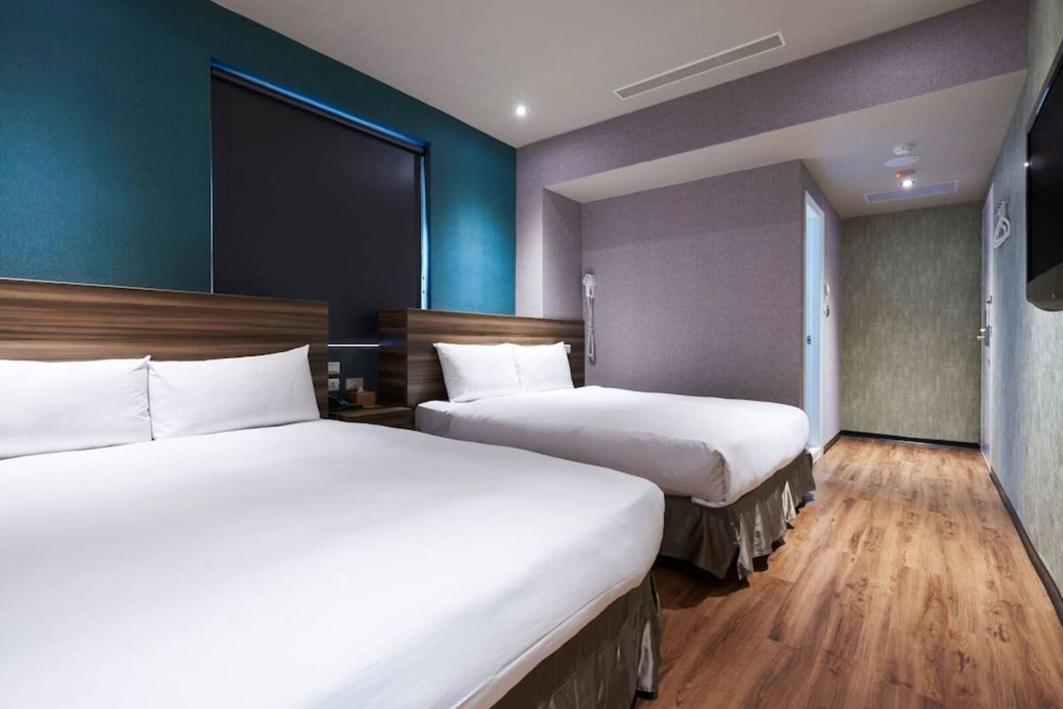 A hotel room with two beds, wooden flooring, and a large window.