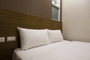 A hotel room with a wooden headboard, white bedding, and a visible power outlet on the wall. - Tomorrow Hotel (Taipei)