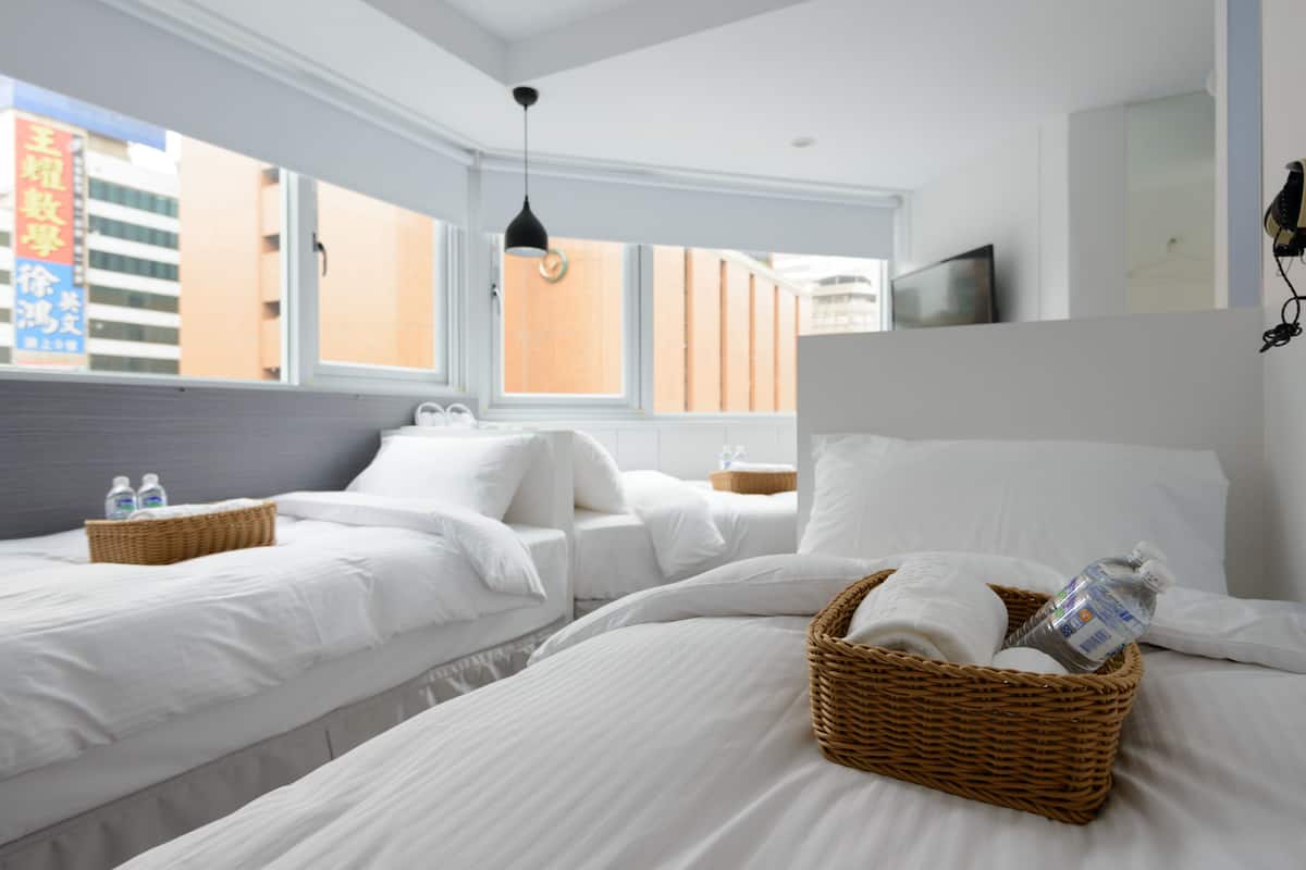 A hotel room with two beds, a large window, and a view of buildings outside.