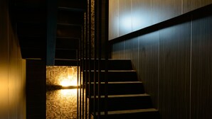 A modern staircase with a wooden finish and metal railings, leading to a lower level with a tiled wall and a light fixture. - Poshpacker Hotel (Taipei)