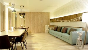 A modern living room with a dining area, wooden flooring, a light blue sofa, and a decorative dog statue. - Poshpacker Hotel (Taipei)