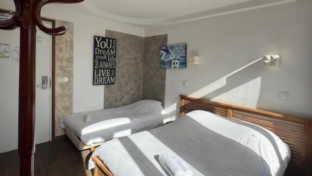 A bedroom with two beds, a wooden coat rack, and a motivational poster on the wall. - Hôtel de France (Lens)