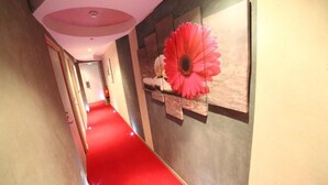 A hallway with a red carpet leading to a room with a large pink flower decoration on the wall. - Hôtel de France (Lens)