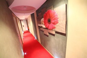 Un couloir recouvert d’une moquette rouge mène à une pièce dont le mur est orné d’une grande décoration florale rose.