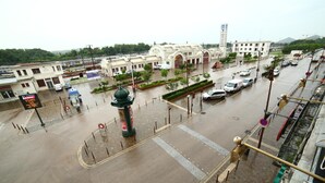 A wet urban square with a central monument, surrounding buildings, and a busy street. - Hôtel de France (Lens)