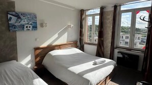 A room with two beds, a desk, and a window with curtains. - Hôtel de France (Lens)