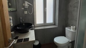 A compact bathroom with a black sink, white toilet, and a window providing natural light. - Hôtel de France (Lens)