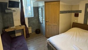 A bedroom with a bed, a desk with a TV, a window, and a door. - Hôtel de France (Lens)