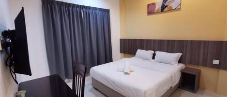 A hotel room with a bed, a desk, a chair, a small table, a wall-mounted TV, and a painting.