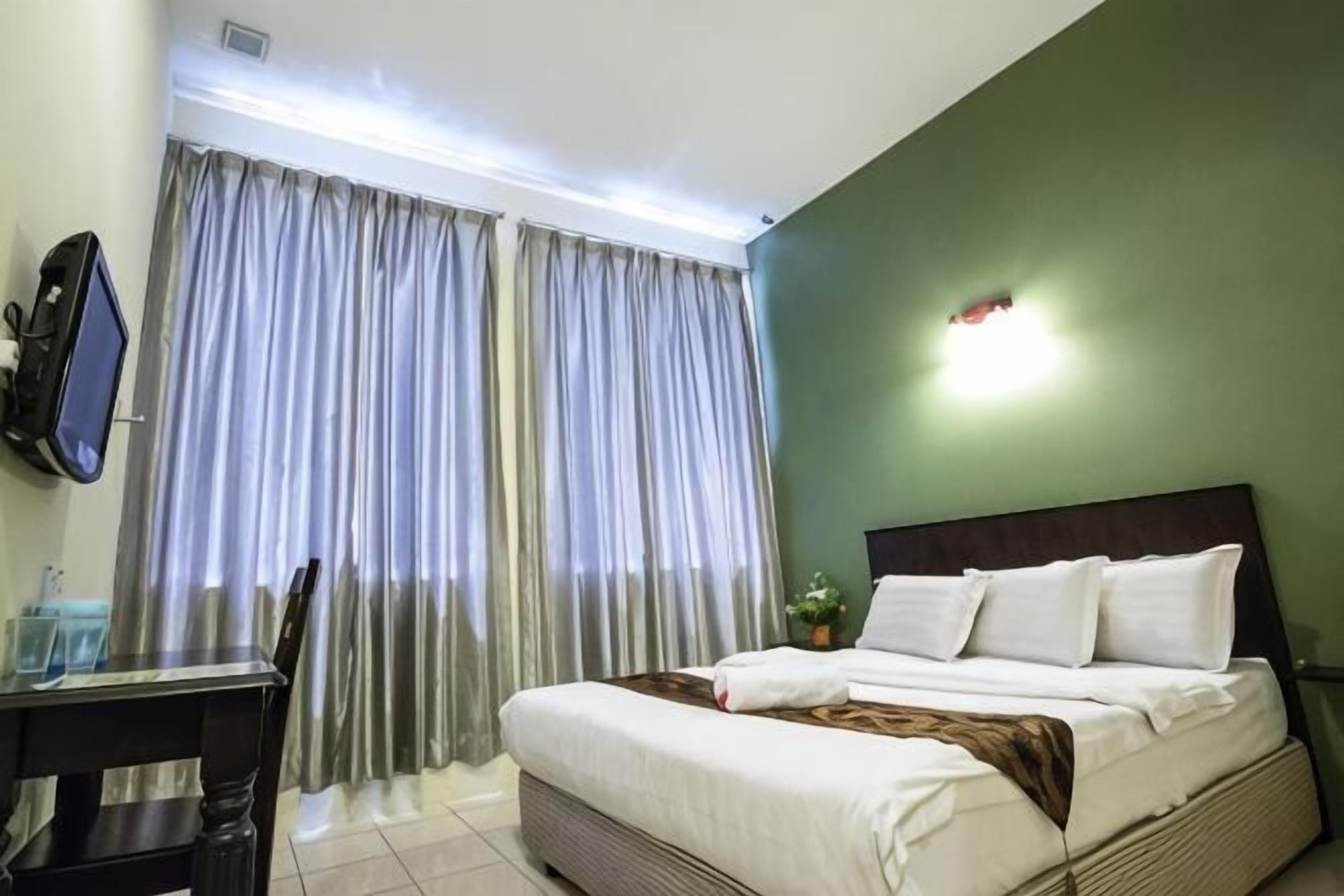 Ein Hotelzimmer mit Bett, Schreibtisch, Stuhl, Fernseher und Vorhängen.