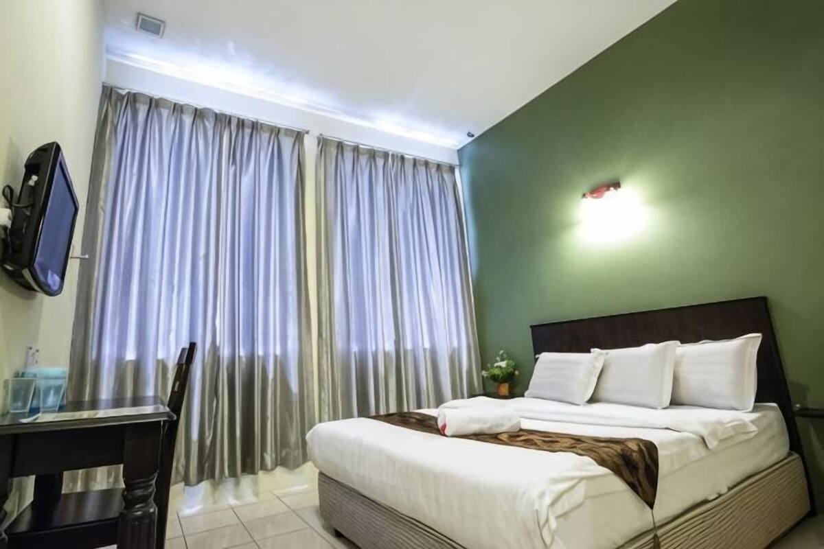 Une chambre d’hôtel avec un lit, un bureau, une chaise, une télévision et des rideaux.