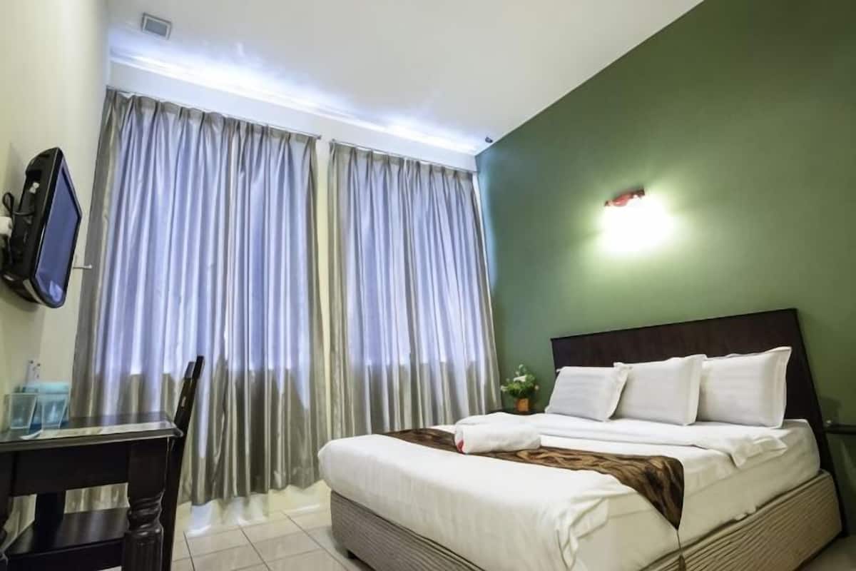 A hotel room with a bed, a desk, a chair, a TV, and curtains.