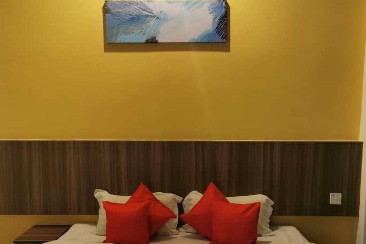Une chambre d’hôtel avec un lit, deux oreillers rouges, une couverture blanche et un tableau au mur.