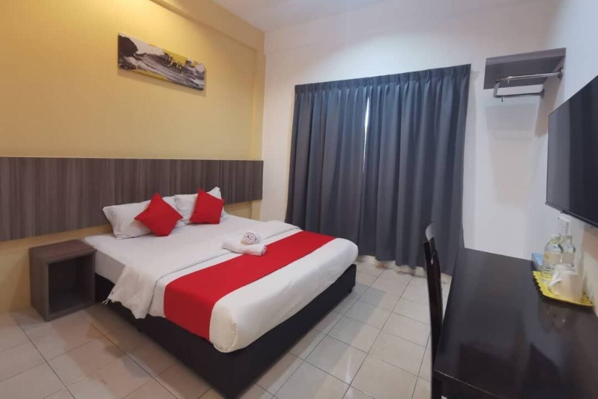 Une chambre d’hôtel avec un lit, un bureau, une télévision et une fenêtre avec des rideaux.