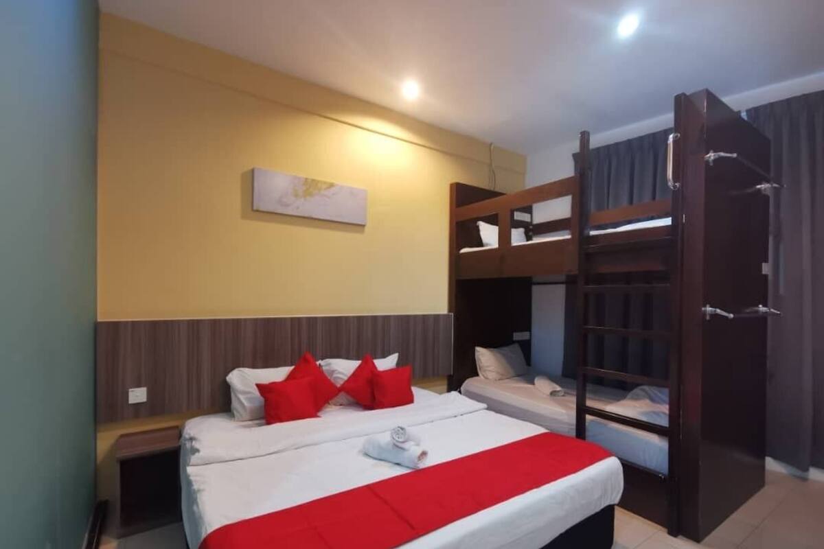 Une chambre d’hôtel avec un grand lit, deux petits lits, un lit superposé en bois, une table de chevet et une commode, ainsi qu’une œuvre d’art accrochée au mur.